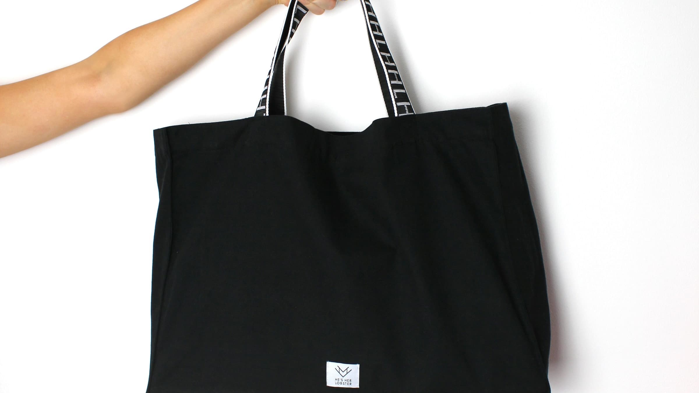 Black tote bag held against a clean studio background